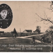 Hiiumaa esimene postiametnik Peet Julge ja vaade Heltermaa sadama suunas. Pildi keskel väikese kuuse tagant paistavad laevamastid. Sellest paremal, sadamasse suunduvast teest vasakul on Heltermaa postijaama hooned, mida enam ammu alles pole. Nende asemel oli vana sadamahoone, mis oli kasutusel enne praegust punase katusega hoonet.